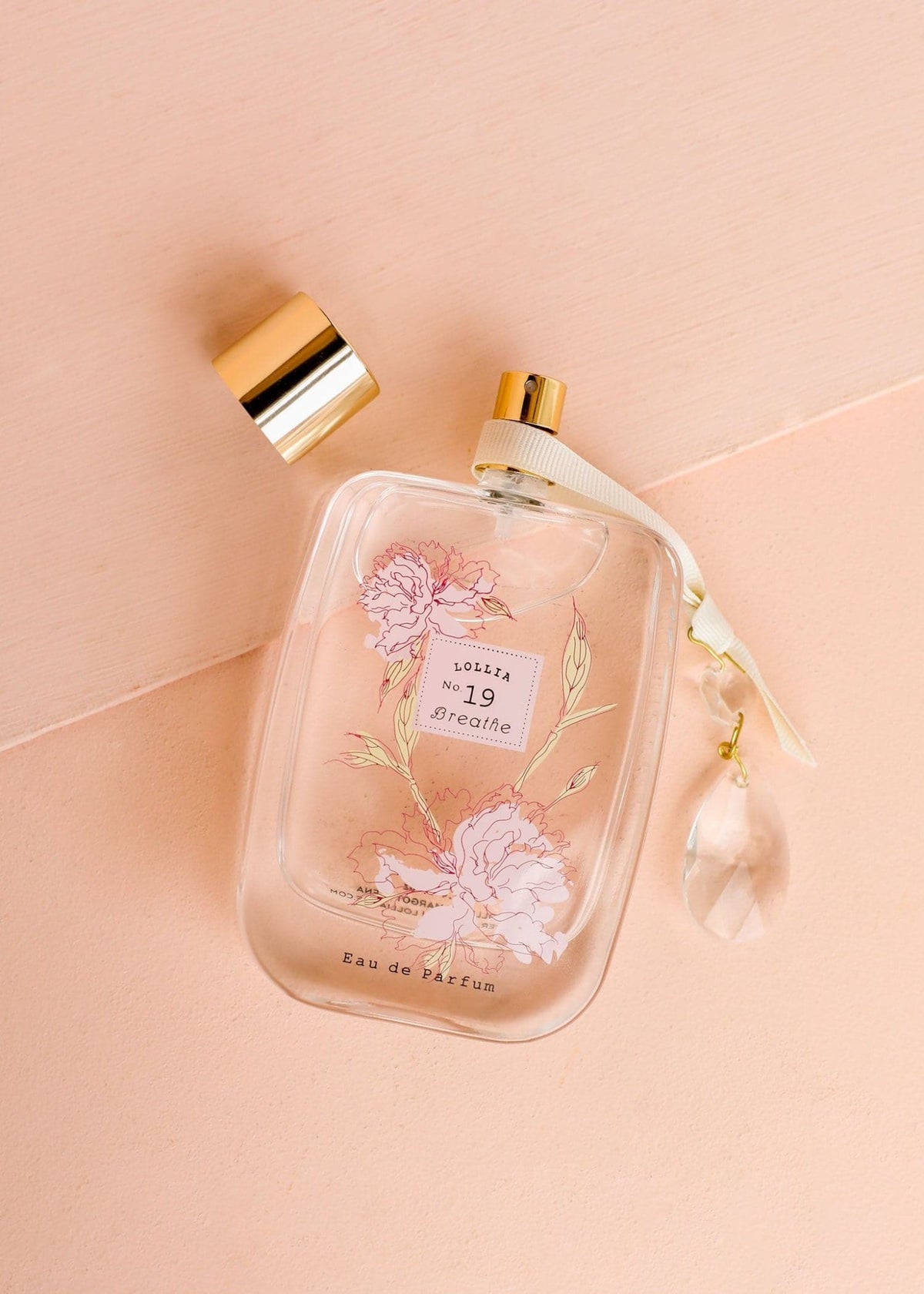 Glass perfume bottle with gold accents, floating peony flowers, satin ribbon tie, and floral heart design.