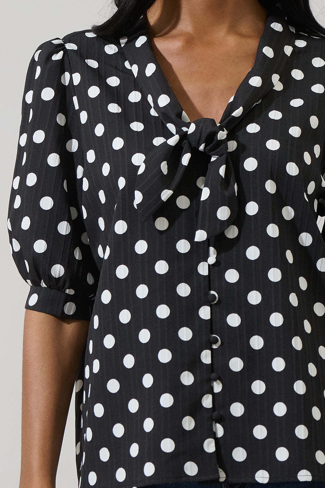 Black polka dot button-down blouse with tie neck and short puff sleeves