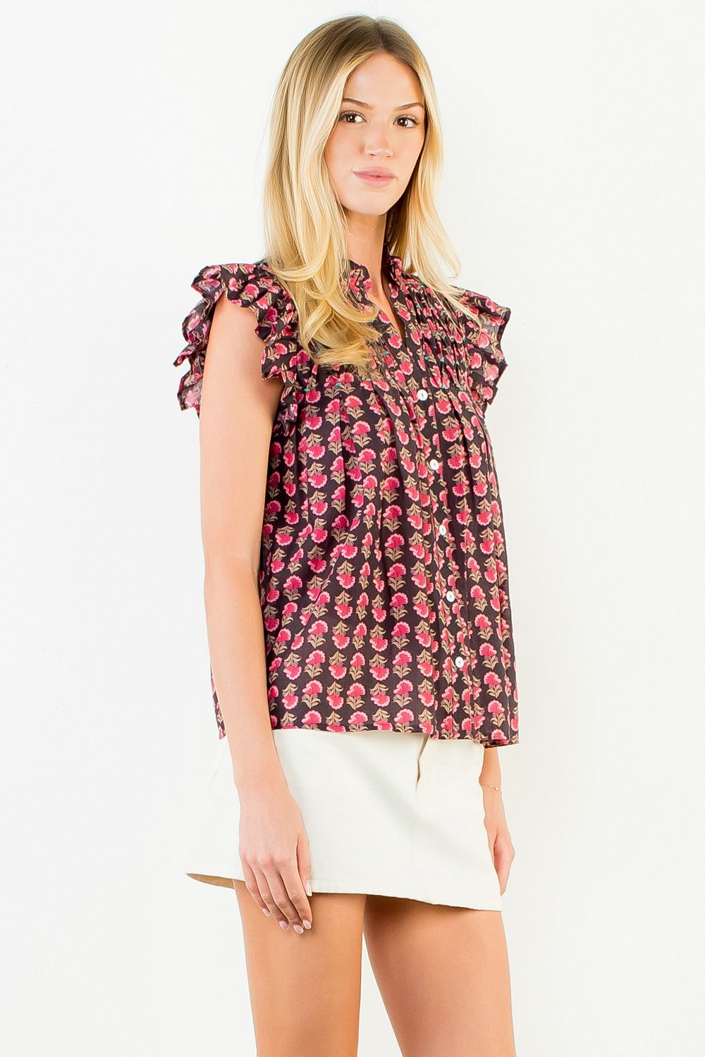 Woman wearing a Jane Flutter Sleeve Button Top with a pink floral print and white mini skirt.
