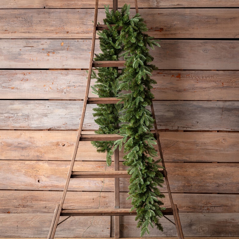 9-foot pre-lit Douglas Fir garland draped over a rustic wooden ladder against a wood plank wall.