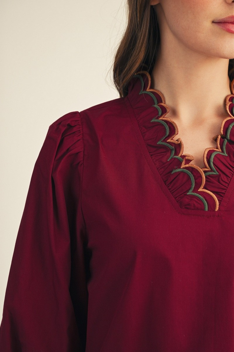 Close-up of a burgundy top with an embroidered scalloped V-neckline and puff sleeves.