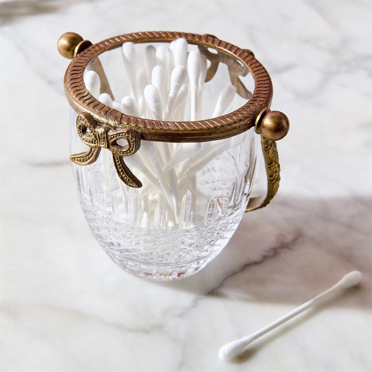 Antique gold finish glass basket with bow accent, filled with cotton swabs on a marble surface.