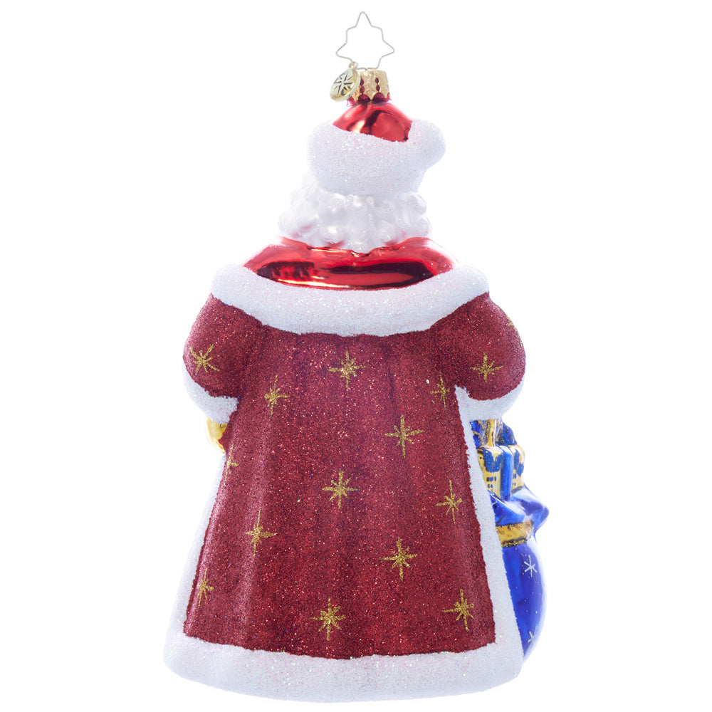 Glass Santa ornament, back view, wearing a red glitter coat with gold stars and white trim, holding a blue gift bag.