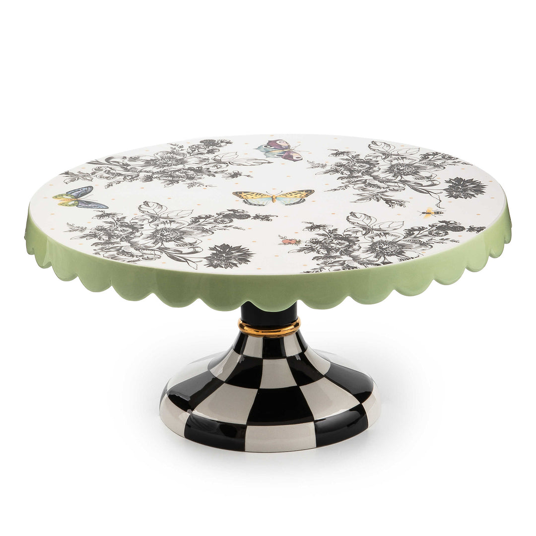 Large ceramic pedestal platter with butterfly toile pattern on checked base and pistachio scalloped edges.
