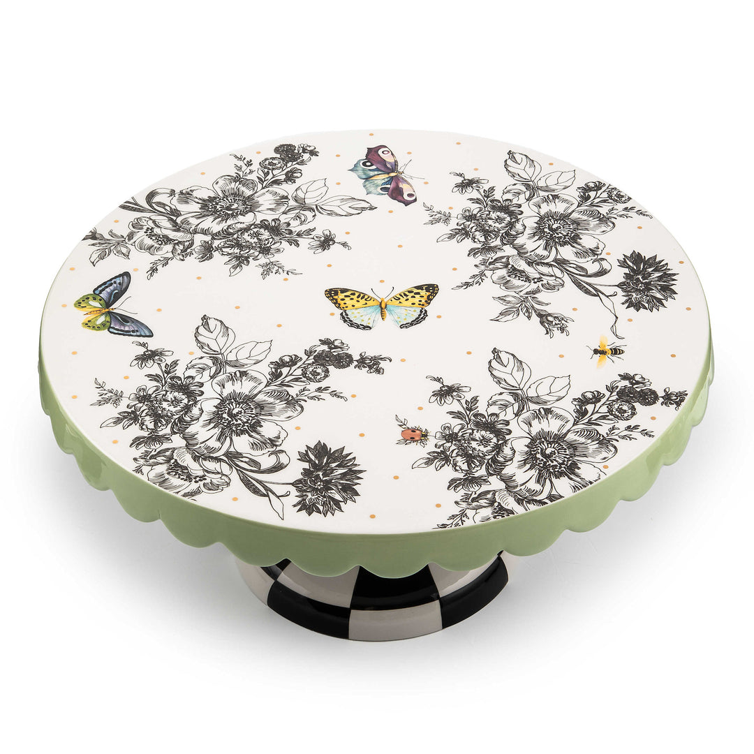 Large ceramic pedestal platter with butterfly toile pattern on checked base and pistachio scalloped edges.