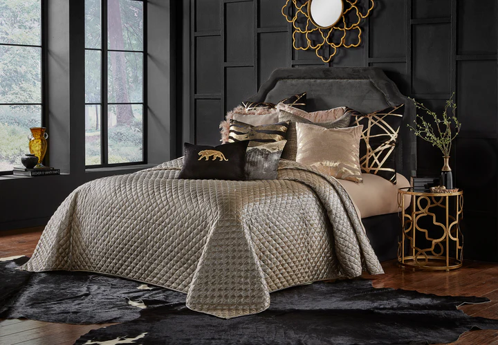 King-size Aura Gold quilted bedspread on a bed with decorative pillows and a black headboard.