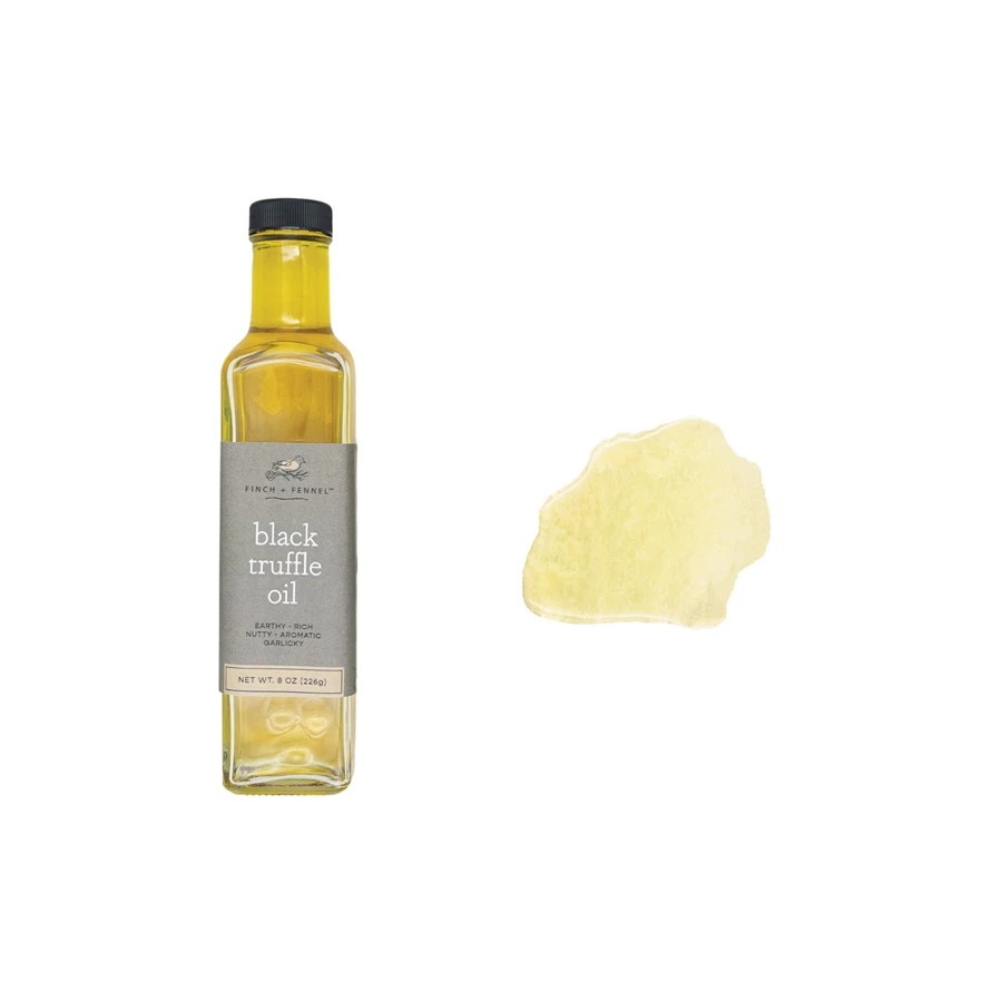 A bottle of Finch + Fennel Black Truffle Oil next to a yellow oil smear on a white background.
