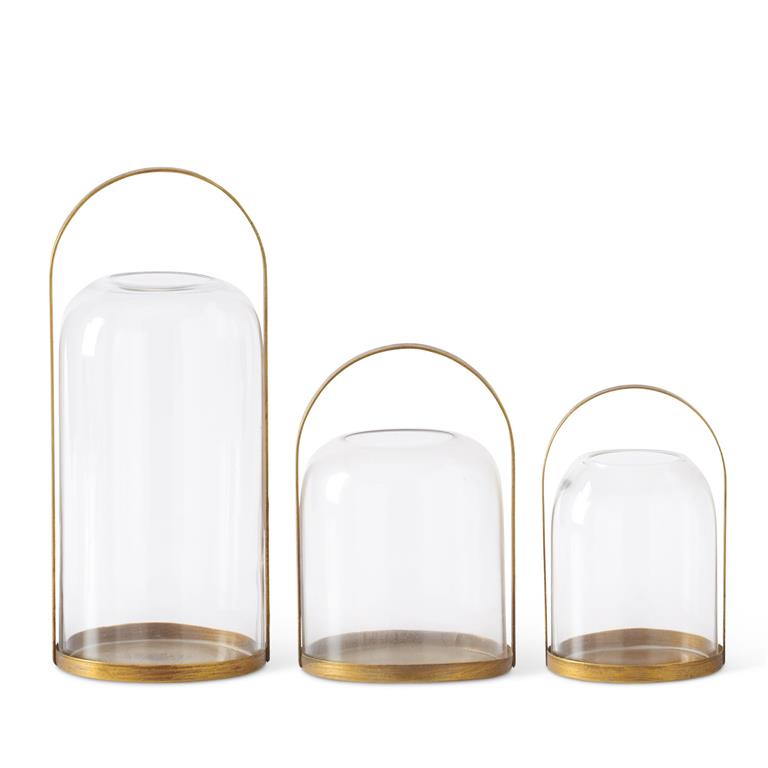 Three round gold metal lantern candleholders with glass domed hurricanes in varying sizes.