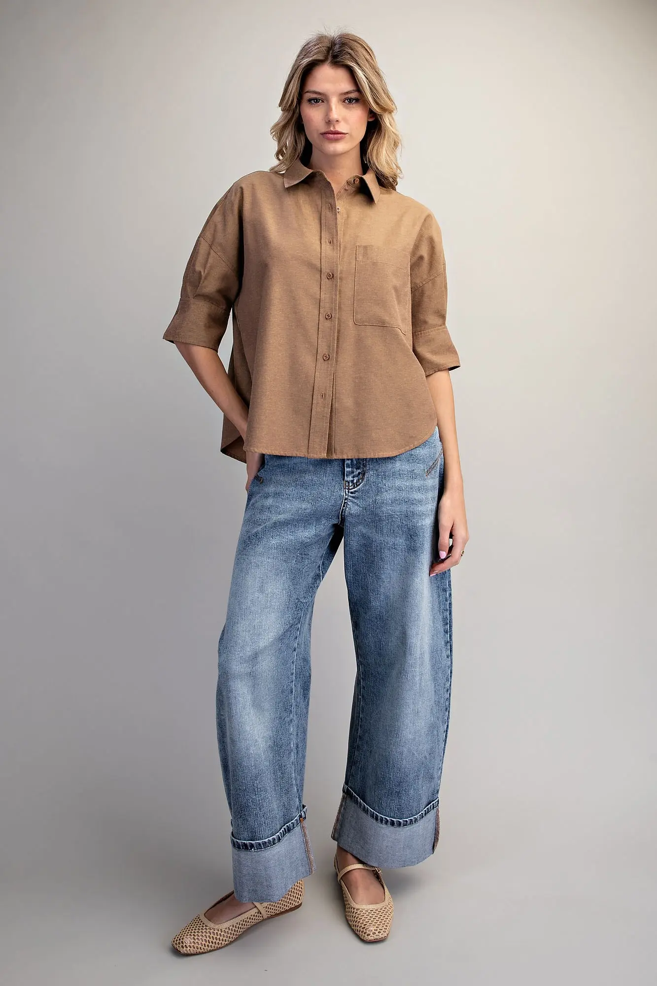 Woman wearing a brown Lou Button Down Short Sleeve Shirt with wide-leg cuffed blue jeans.