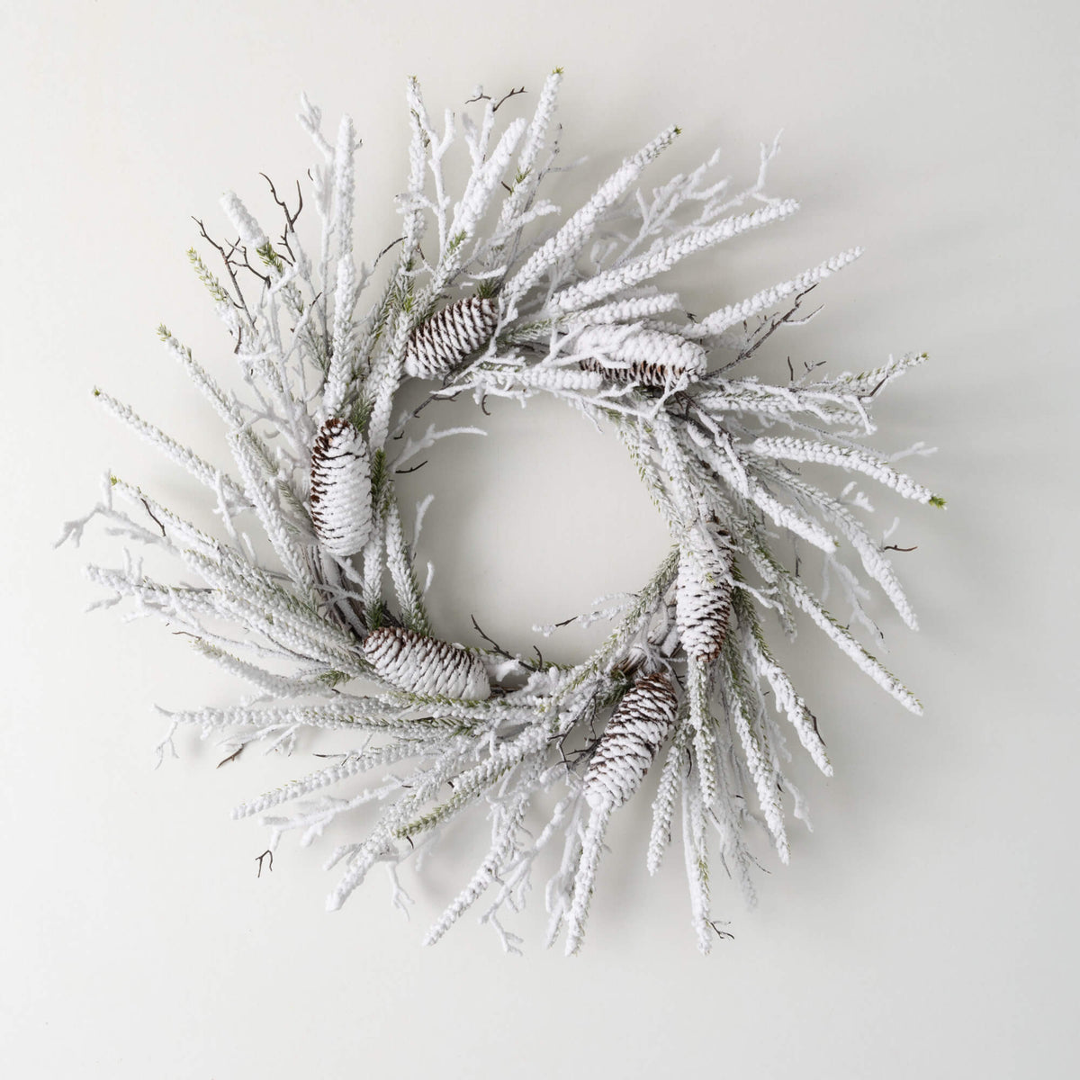 A 24-inch flocked pine twig wreath with snow-covered branches and pinecones on a white background.
