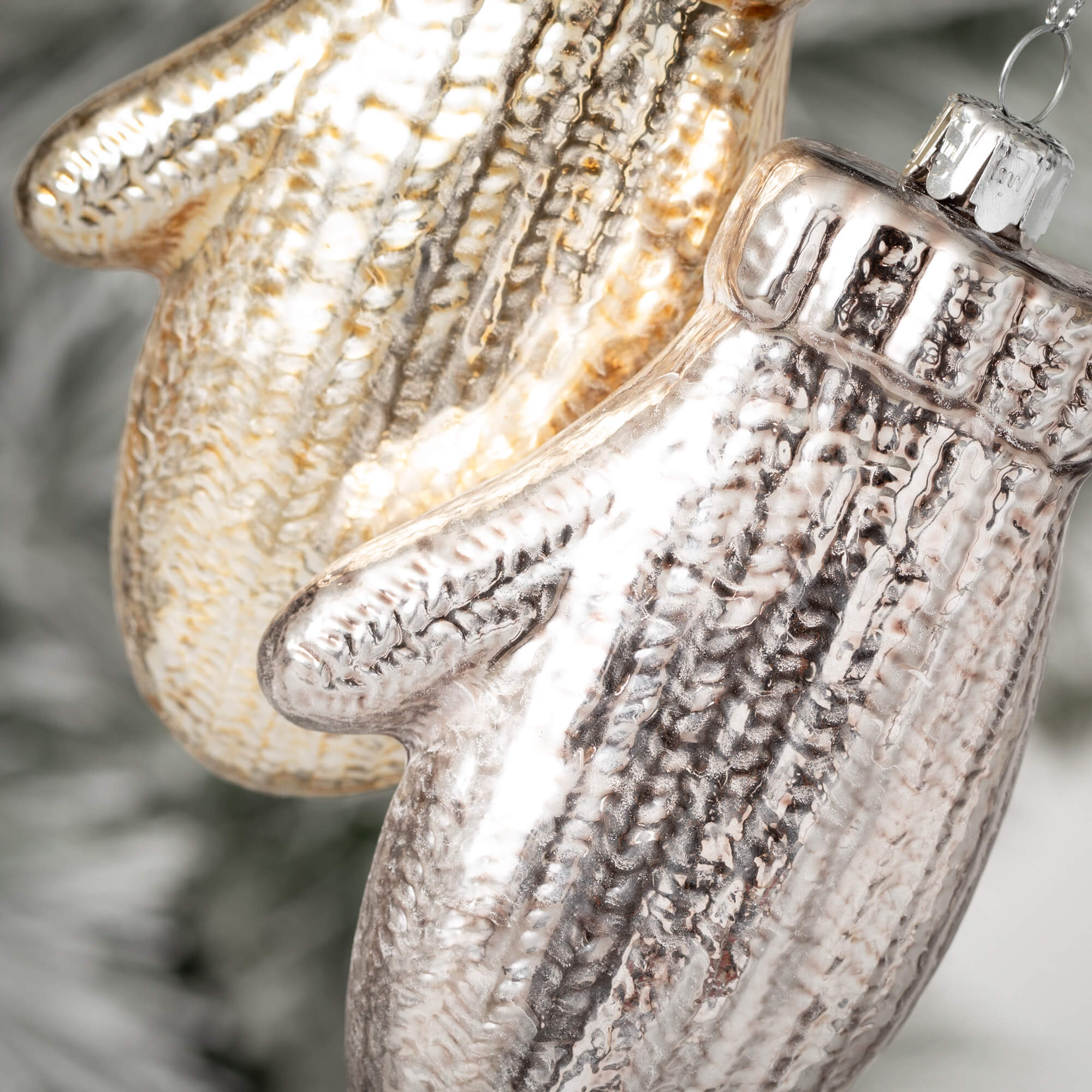 Close-up of two glass brushed mitten ornaments in gold and silver with a knit texture.
