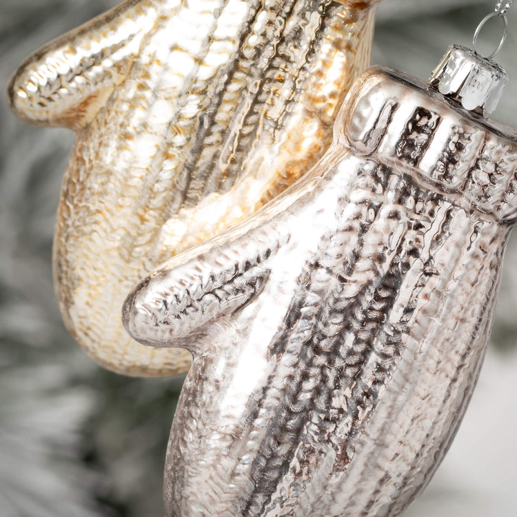Close-up of two glass brushed mitten ornaments in gold and silver with a knit texture.