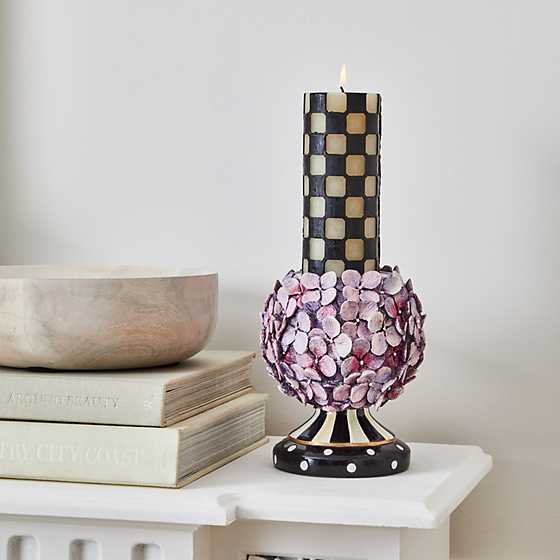 A 6-inch black and cream checkered pillar candle lit on a decorative floral hydrangea candle holder.