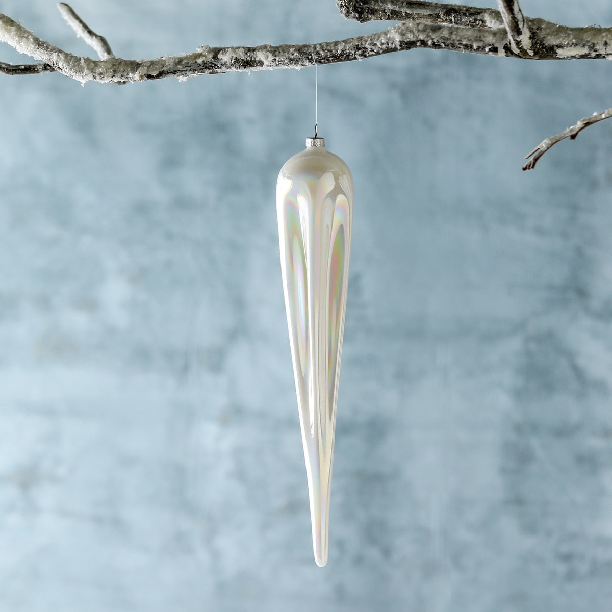 Frosty pearl glass icicle ornament with an iridescent finish hanging from a snowy branch.