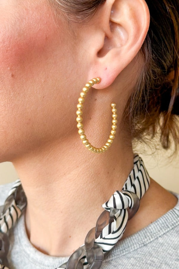 A person wearing a gold WS Grace Hoop Earring featuring a beaded texture design.