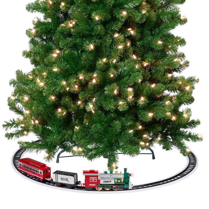 A toy train set with a red engine and cars on a circular track around a lit Christmas tree.