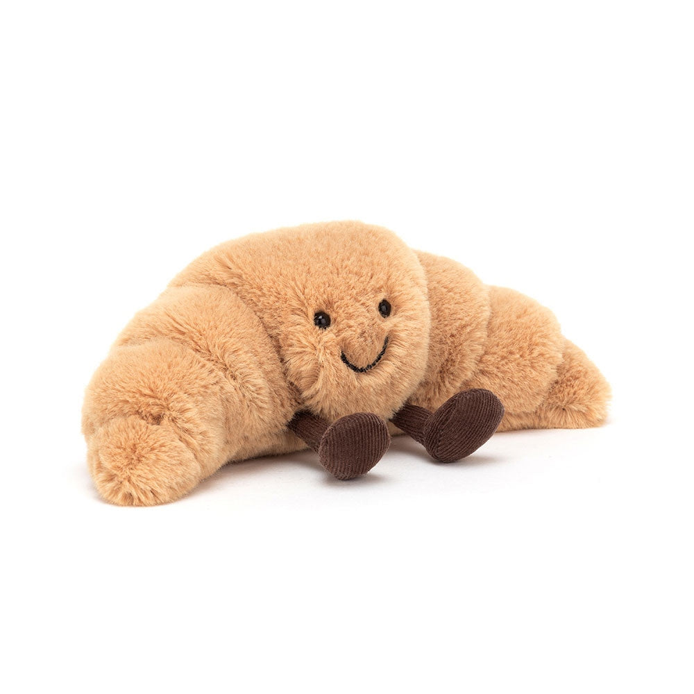 Amuseables Croissant plush toy in beige polyester with a smiling face, bow tie, and chocolate tray accessory.