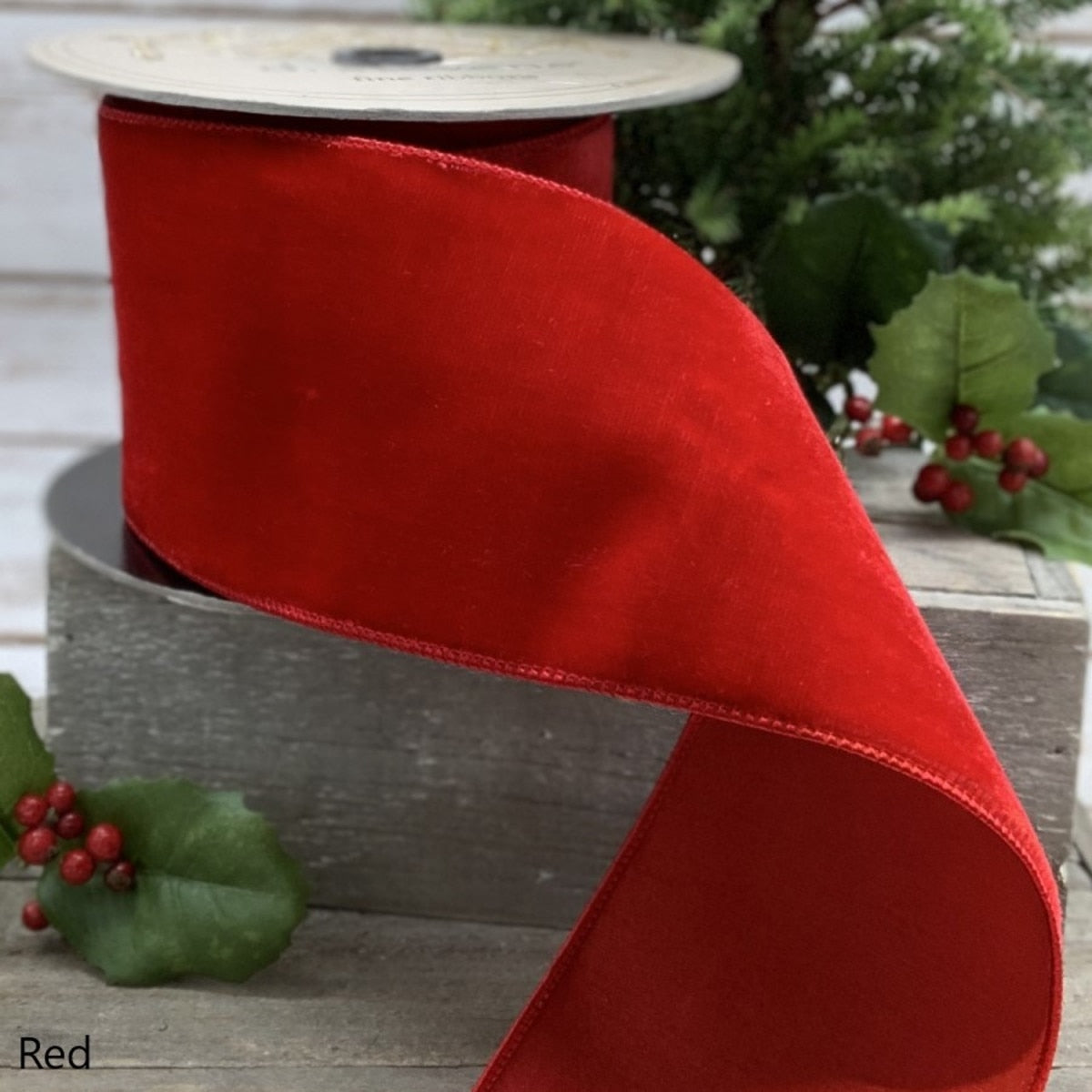 A spool of 4-inch wide red velvet ribbon with a smooth texture, displayed with holly accents.