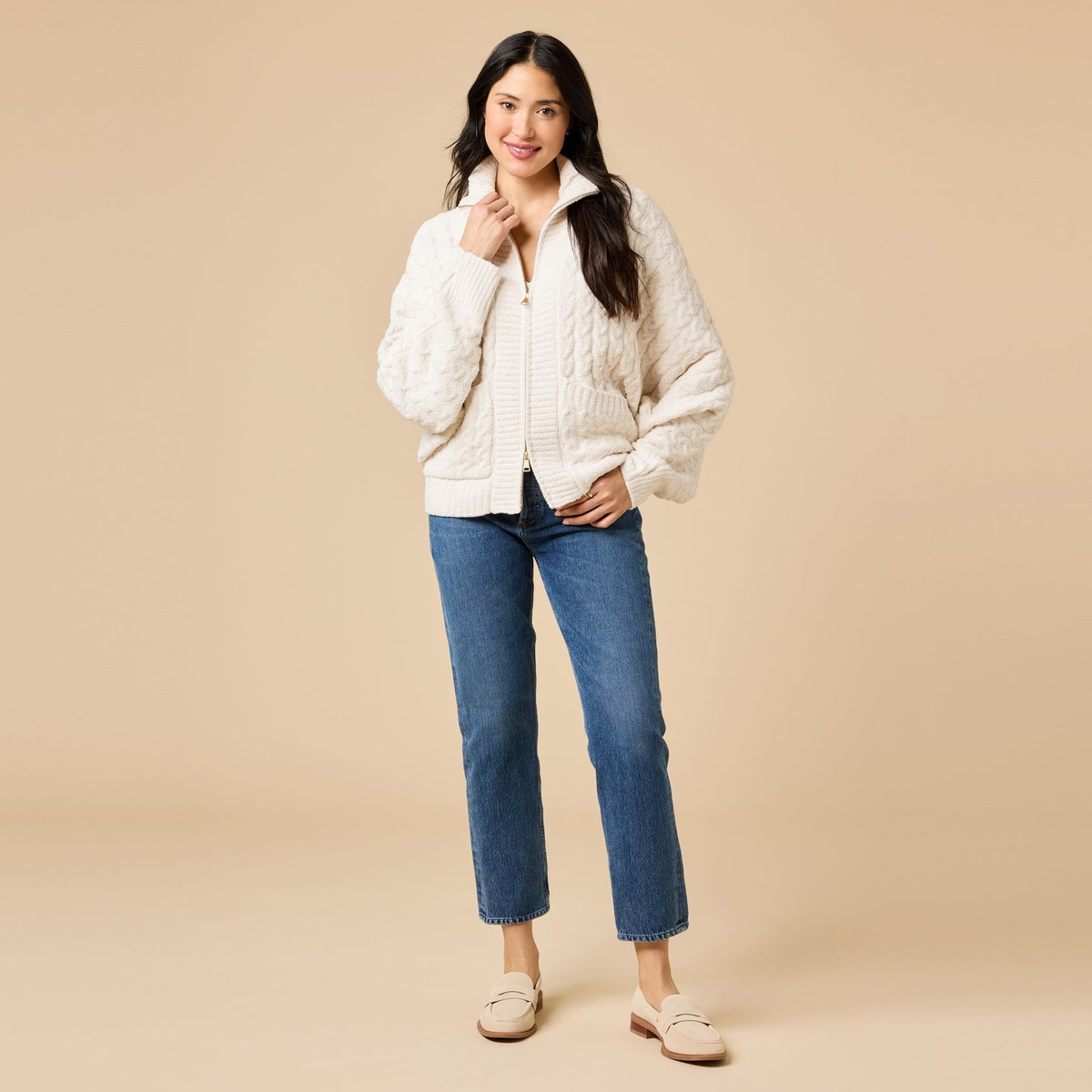 Woman wearing a cream Cable Knit Marshmallow Funnel Neck Double Zip Jacket with blue jeans.