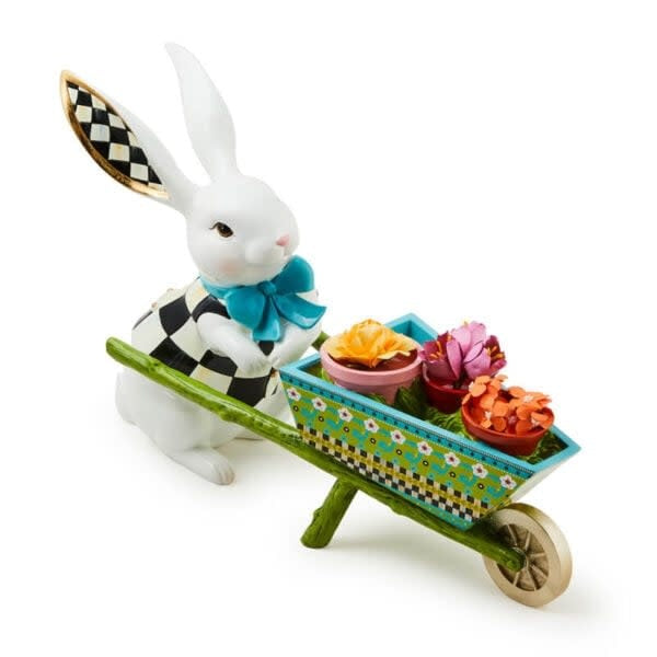 Calico bunny figurine standing beside a small wheelbarrow resin sculpture with striped pattern.