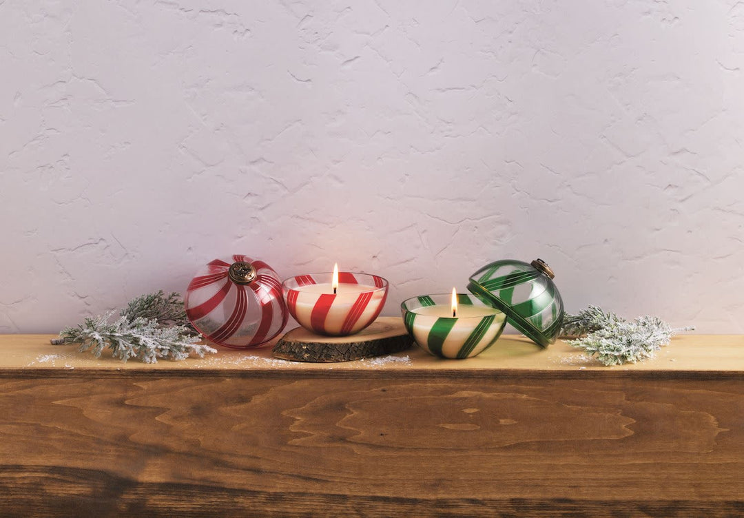 Glass ornament candle with lid in candy cane red and white stripes, smoked cedar scent.