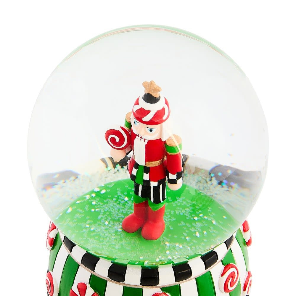 Resin snow globe featuring a candy cottage nutcracker soldier with red hat inside clear glass sphere.