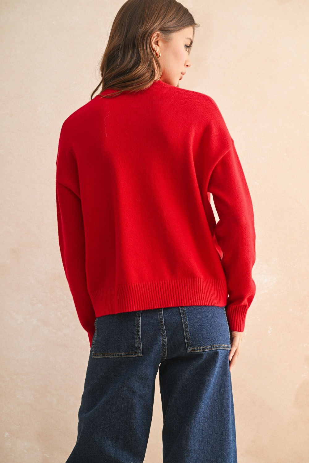 Back view of a woman wearing a red crew neck sweater with ribbed hem and dark blue jeans.