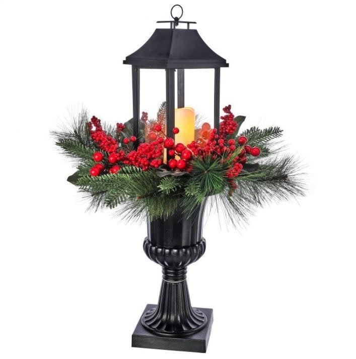 Black lantern urn with LED candle, red berries, and green pine needles for holiday decor.