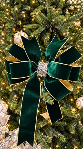 Emerald green velvet holiday bow with gold trim and a rhinestone center on a Christmas tree.