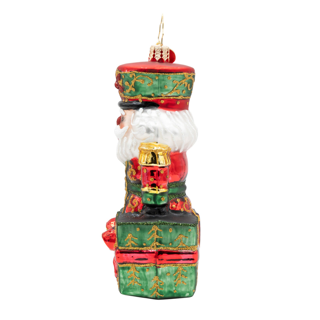 Side view of The Gifted Guard nutcracker glass ornament emerging from a green and red gift box.