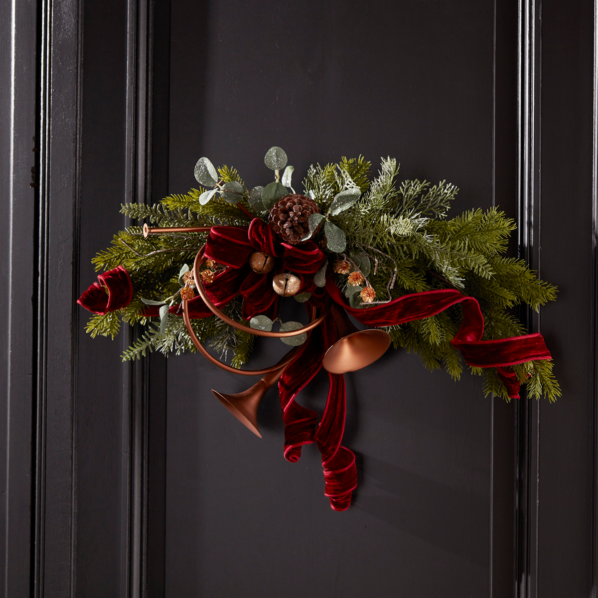 11-inch metal horn ornament with pine branches, pinecones, and red velvet ribbon on a black door.