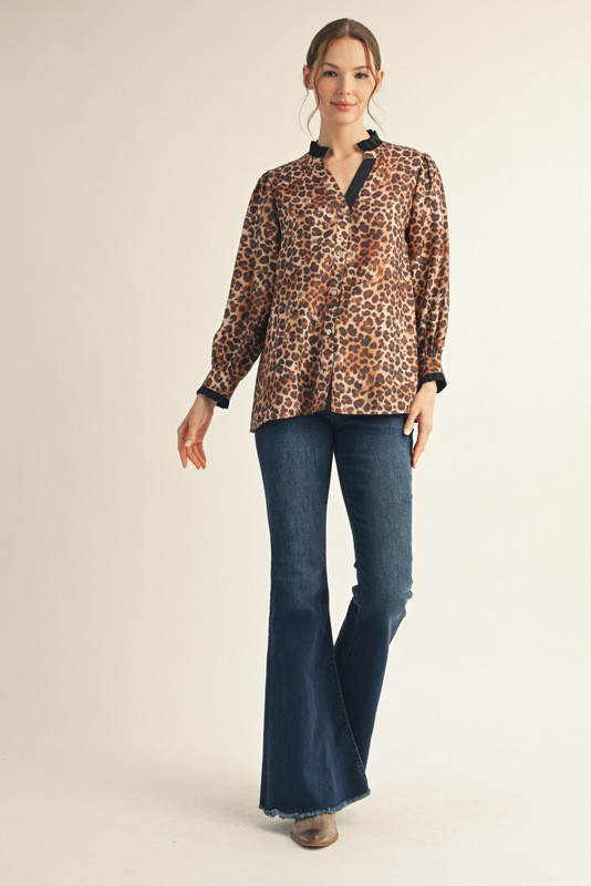 Woman wearing a long sleeve leopard print button-down top with a ruffled neckline and dark jeans.