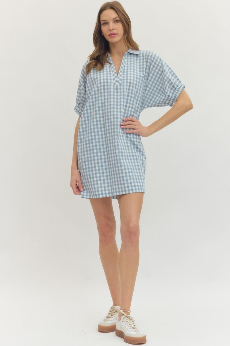 Woman wearing a light blue and white gingham short sleeve mini dress with white sneakers.