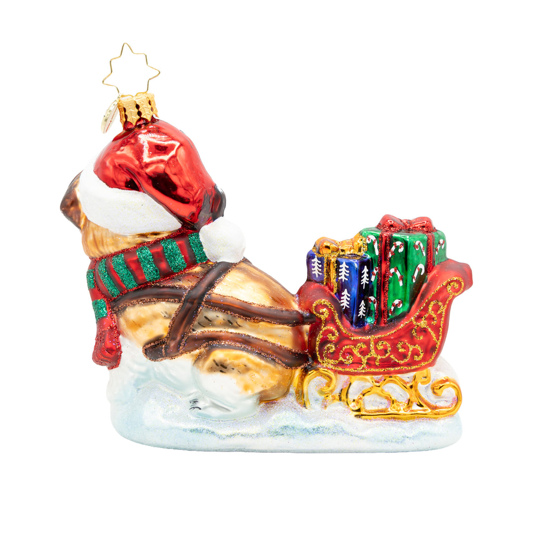 Glass dog ornament wearing a Santa hat and scarf pulling a red sleigh filled with gifts.