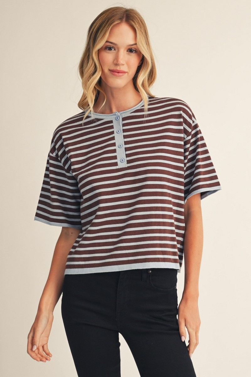 Woman wearing a brown and light blue striped short sleeve henley sweater top with black jeans.
