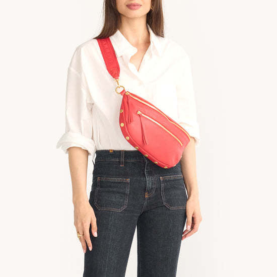 Oxblood red pebble leather crossbody bag with adjustable strap, gold hardware, and front zippered pocket.