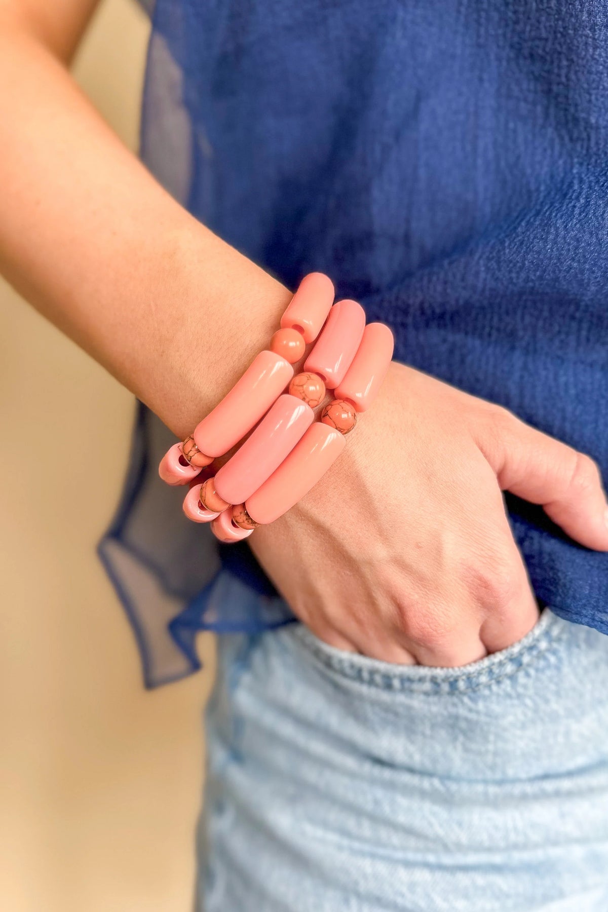 A person wearing a stack of pink WS Emmy Bracelets featuring large acrylic tubes and marbled beads.