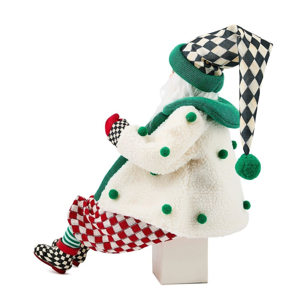 Handmade fabric Santa figurine in red check pants with a cozy cardigan resting on an end table.