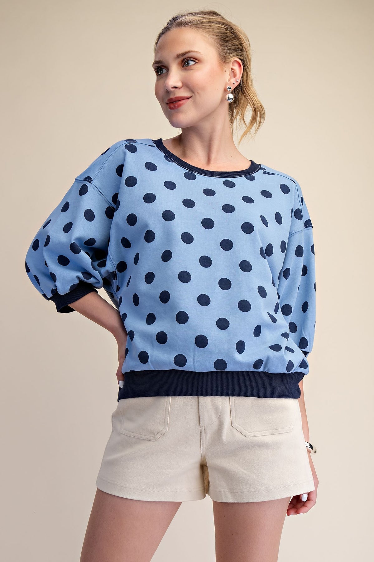 Woman wearing a light blue round neck sweatshirt with navy polka dots and bubble sleeves.