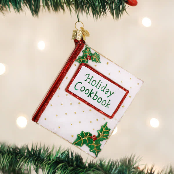 Glass Christmas ornament shaped like a red cookbook with gold trim.