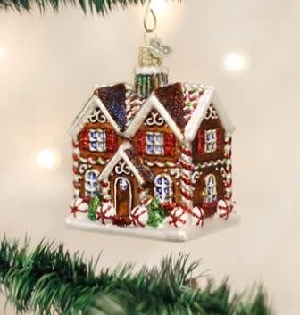 Glass cottage ornament with white walls, red roof, green door, snow-covered ground, and festive lights.