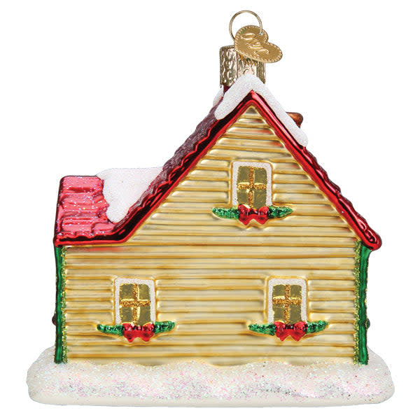 Glass Christmas cottage ornament with red roof, white walls, green door, snow-covered ground, and festive lights.