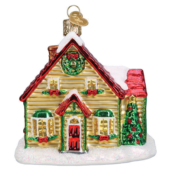 Glass Christmas cottage ornament with white walls, red roof, green door, snow-covered ground, and a chimney emitting smoke.