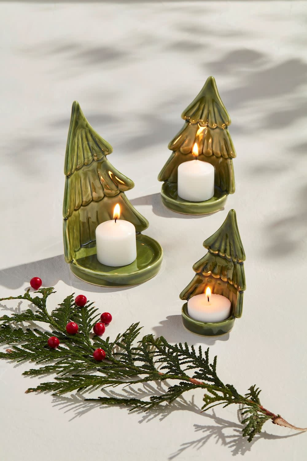 Set of three hand-painted green stoneware Christmas tree votives with tea light plates.