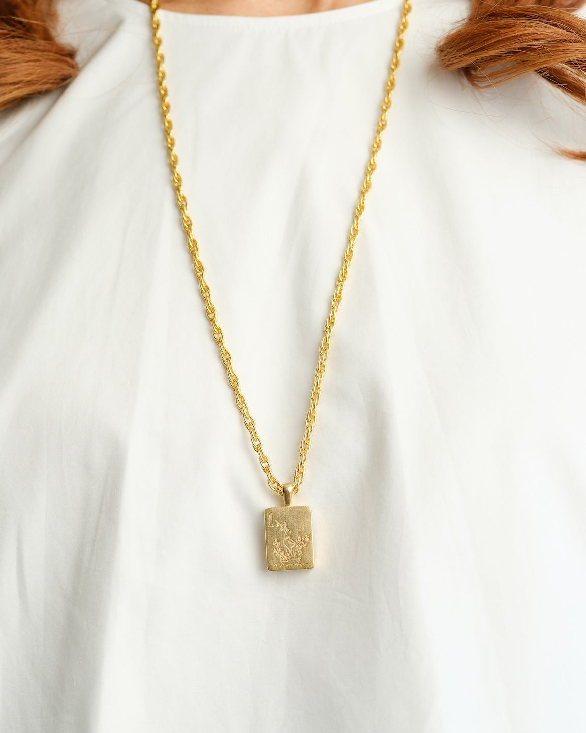 A person wearing a long 24K gold triple-plated chain with a Bird Bam mahjong tile pendant.