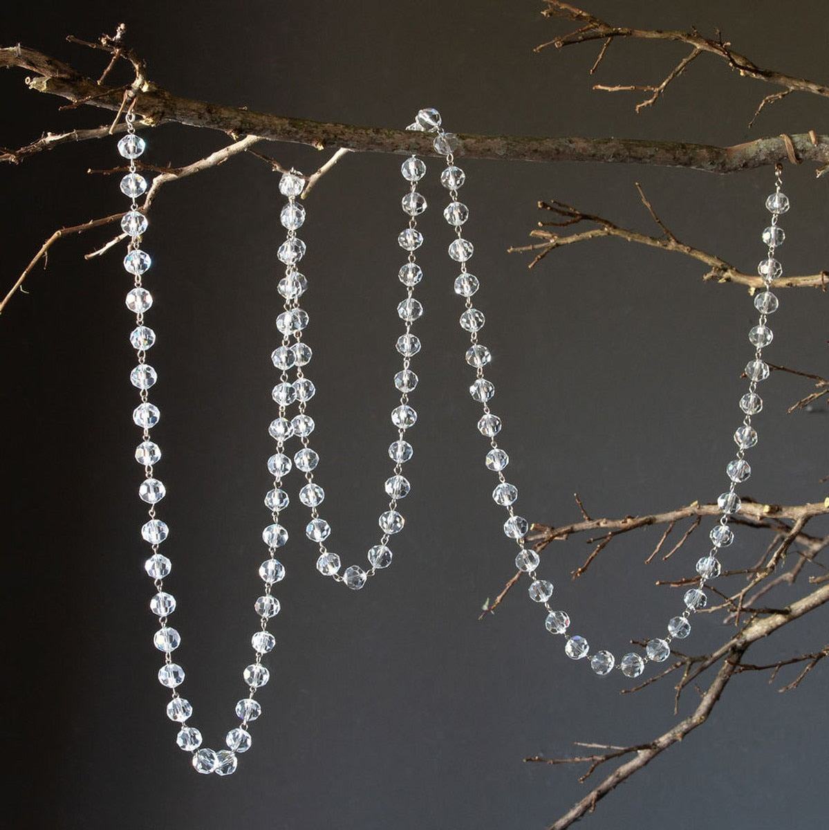 70-inch faceted glass crystal garland draped over a rustic tree branch against a dark background.