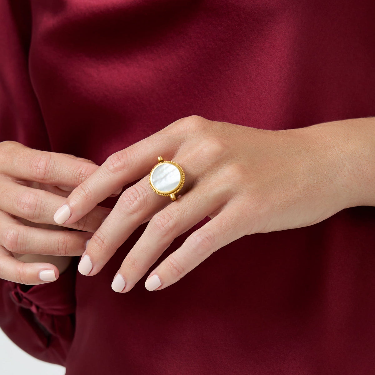 A person wearing a gold revolving ring with a circular mother of pearl inlay on their middle finger.