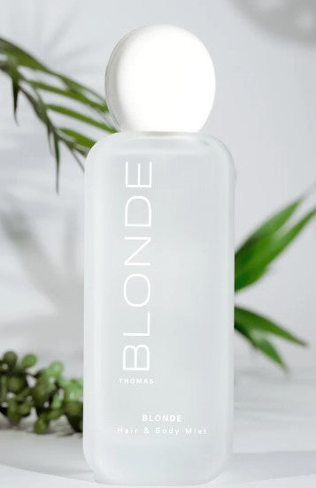 Frosted glass bottle of Blonde Hair & Body Mist with a white spherical cap against a leafy backdrop.
