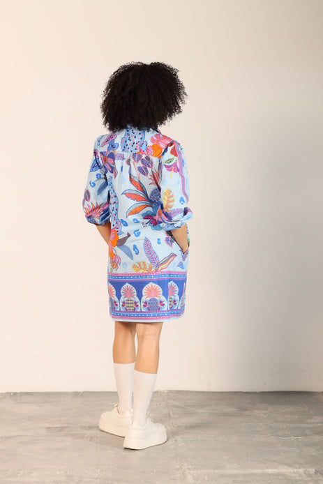 Light blue midi dress with a colorful floral print and a blue patterned hem, worn by a woman with curly hair.