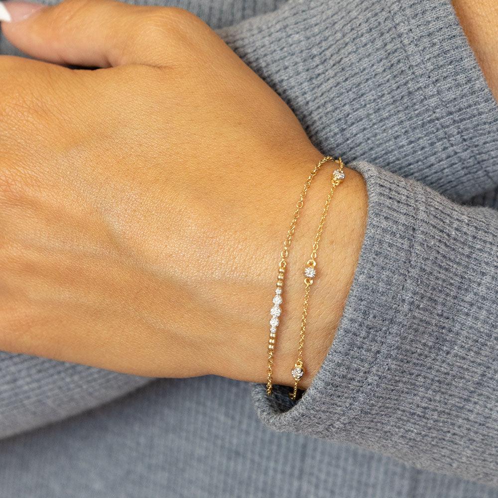 A person wearing two delicate gold Beaded Connection Chain Bracelets with small diamond accents.